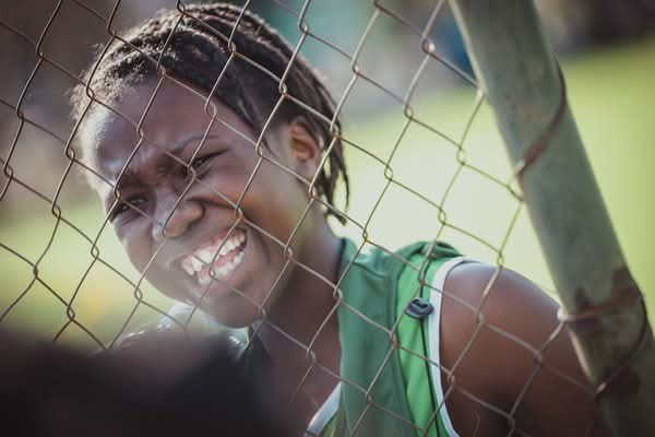 Young athlete smiling through the fence